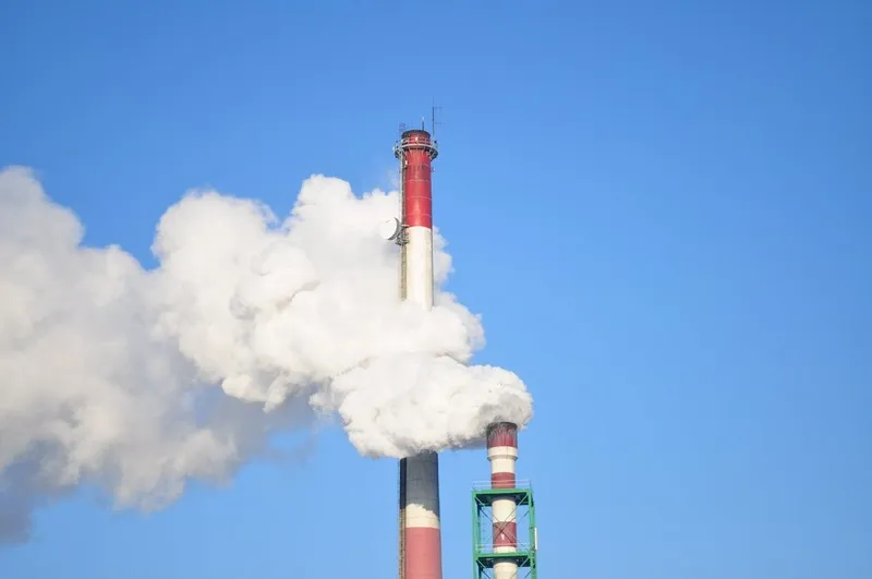 Industrial smokestacks emitting pollution into the sky symbolizing the environmental impact of ecommerce returns and the need for sustainable reverse logistics.
